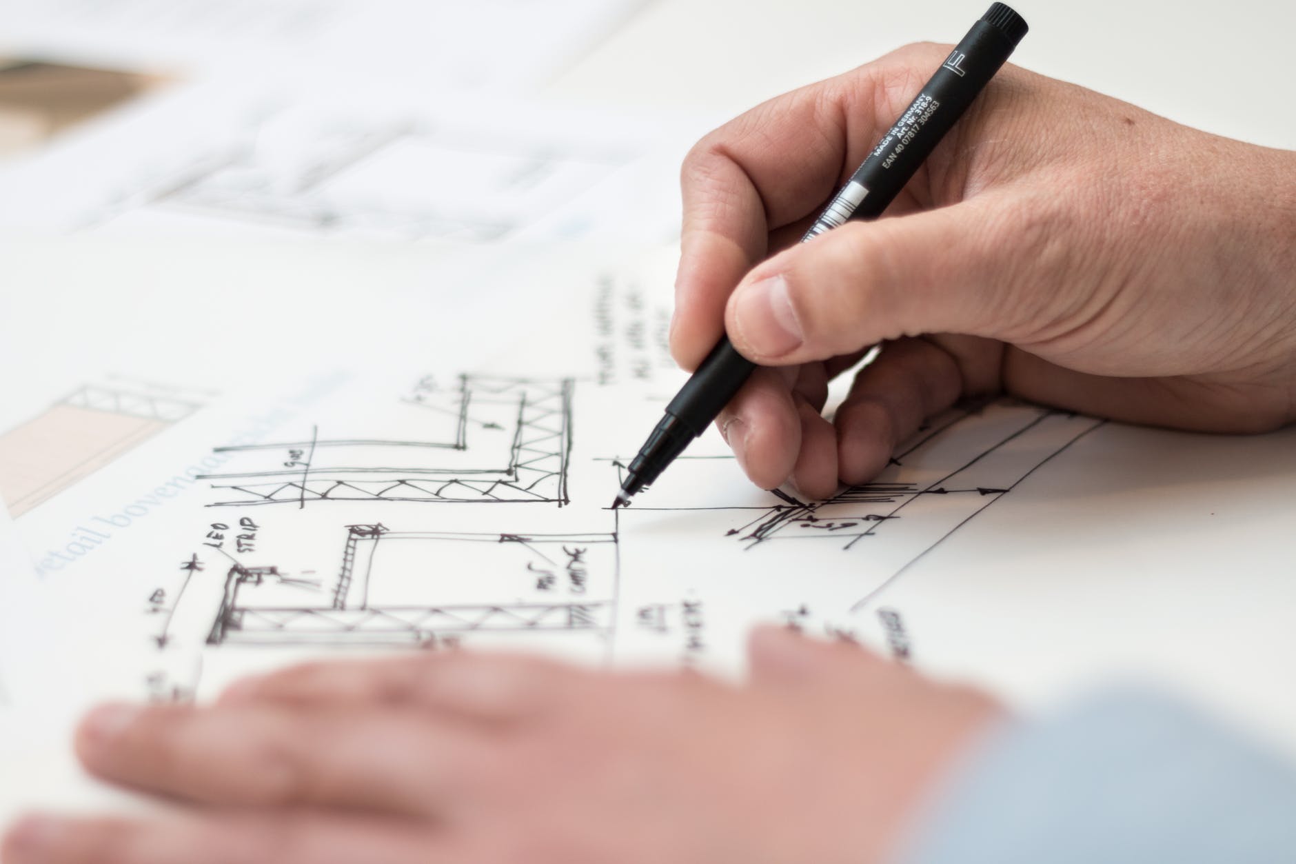 An image of hands that are holding a pen going over architecture plans