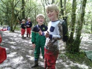 Two school children smiling at the camera covered in mud