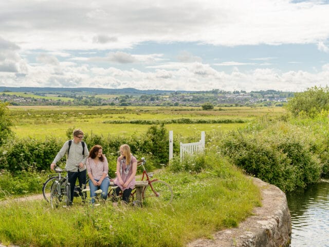 3 young adults with their bikes in the foreground. The background is the rolling hills of Devon