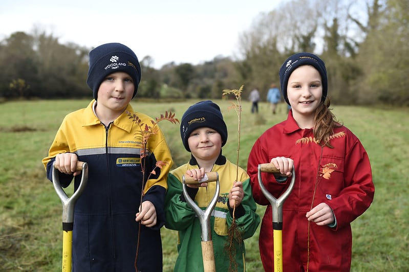 Three children holding a spade each and some tree saplings on an Autumn day