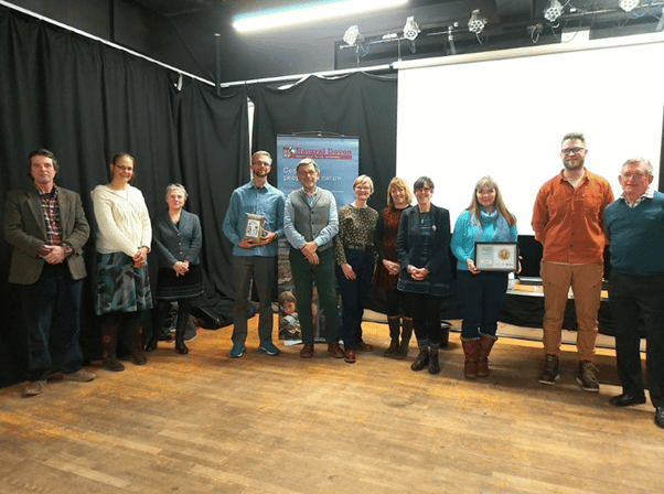 Nine people pose for a photograph, holding awards