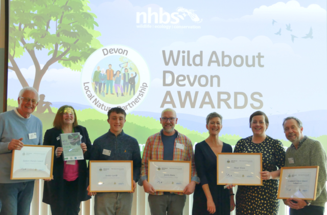 Five award winners hold certificates with Nora Corkery in front of a Wild About Devon slide