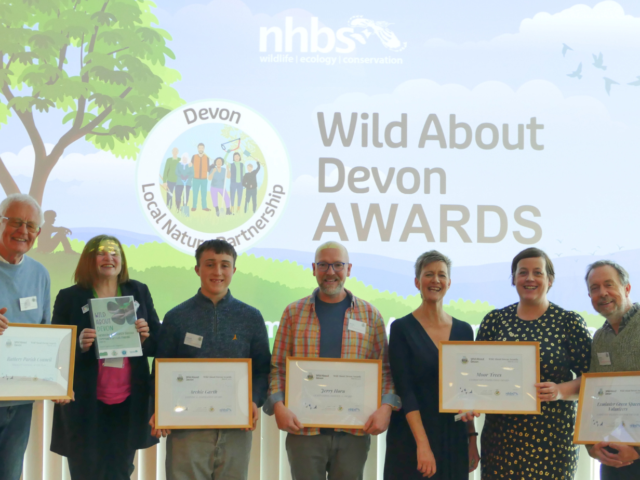 Five award winners hold certificates with Nora Corkery in front of a Wild About Devon slide