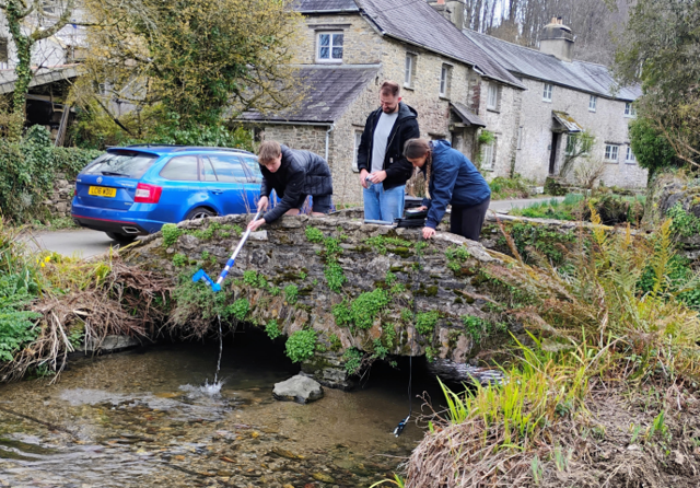 A group of people sample river water from the bridge above